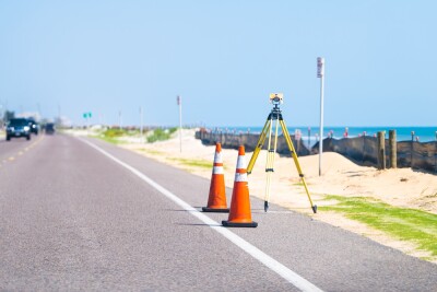Construction surveyor equipment theodolite level tool at road highway asphalt paving works with cars in background in Hammocks, Florida by Atlantic ocean