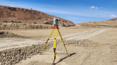 A solitary surveyor's tripod standing tall in the vast expanse of a dirt field, symbolizing precision and accuracy in mapping out the terrain